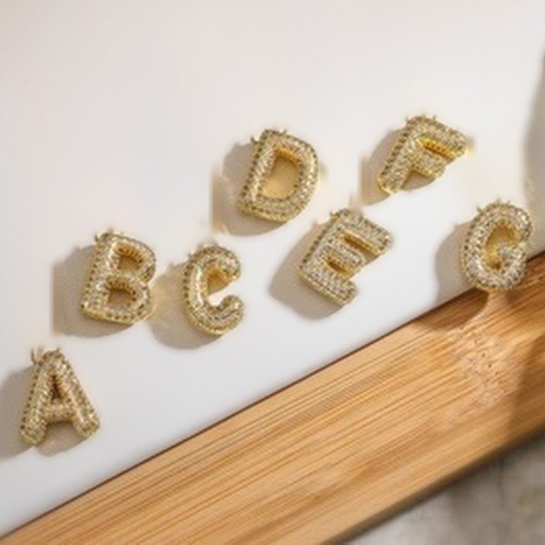 Gold pavé bubble letter pendants A to G resting against a white wall